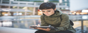 Young Woman with short dark hair sitting outdoors looking at tablet