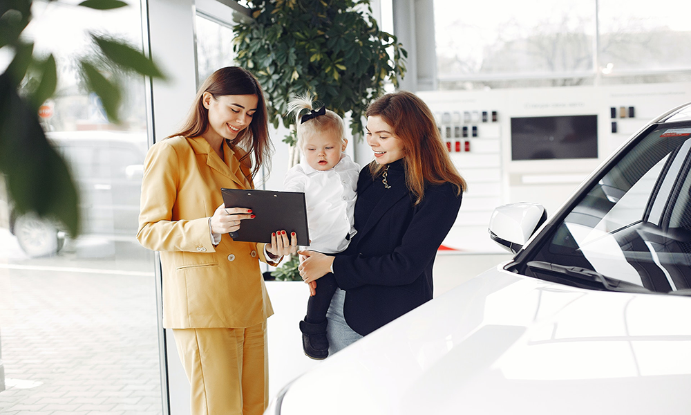 woman holding baby looking at tablet held by woman in yellow suit