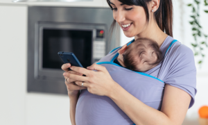 young woman cuddling baby holding cell phone