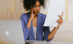 Young Woman Wearing Glasses Sitting At Desk Looking At Paper