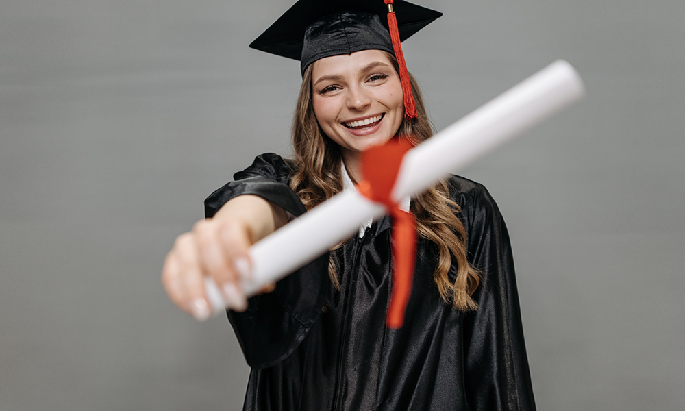 Young Woman In Grad Cap And Gown Holding Paper