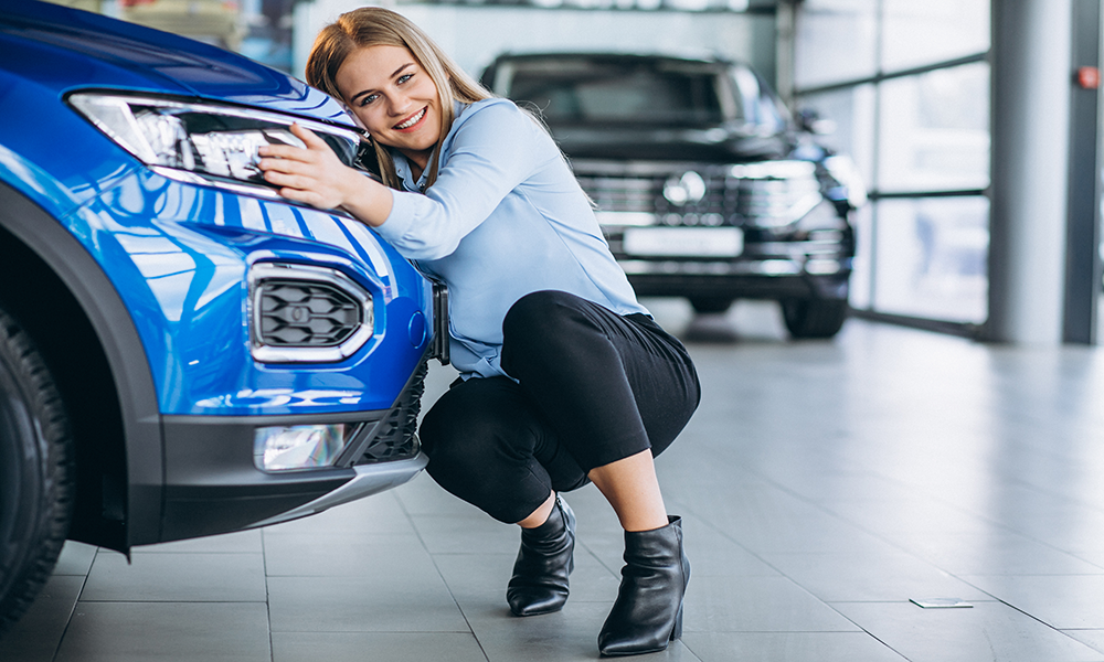 Smiling Young Woman Hugging Bumper Of Blue Vehicle