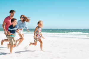 Cheerful Young Family Running On The Beach.