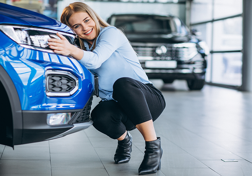 Smiling Young Woman Hugging Bumper Of Blue Vehicle