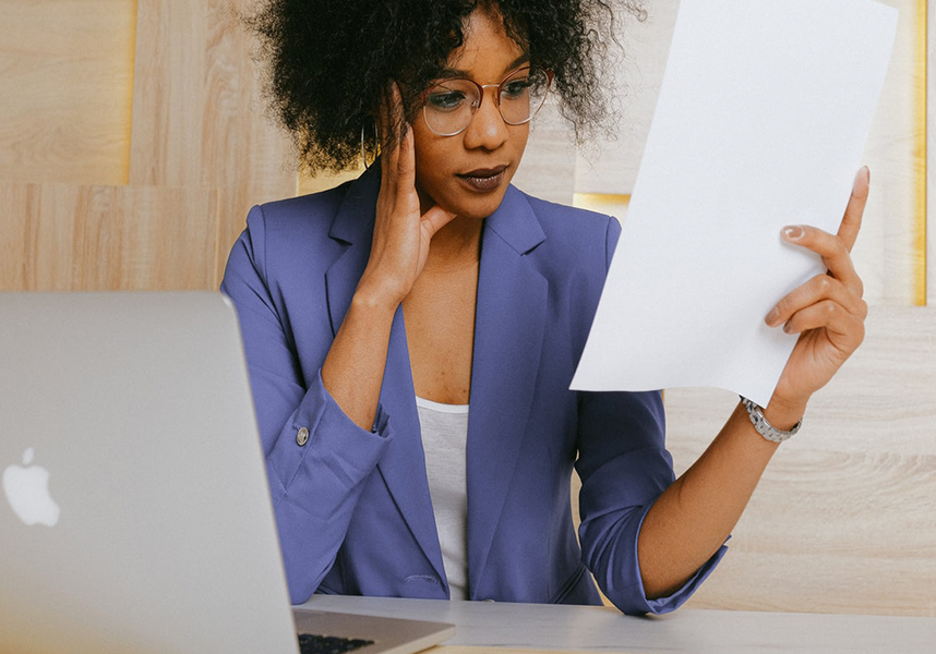 Young Woman Wearing Glasses Sitting At Desk Looking At Paper